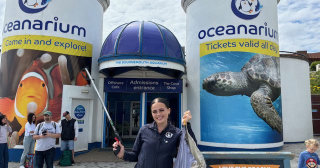 Lay holding feeding stick and bag in front of Bournemouth Oceanarium.